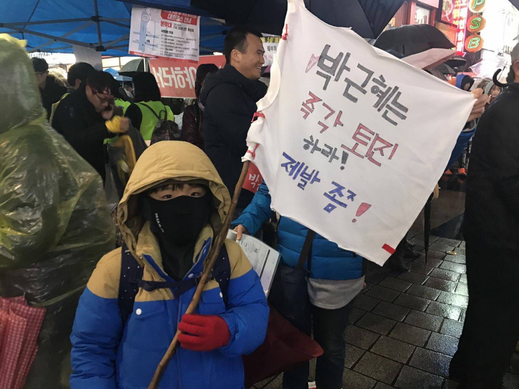 參與示威遊行的韓國小學生手拿旗幟,白色布條寫著「朴槿惠趕快下臺吧!就拜託您了,真的!」樹枝做的旗杆有揭竿起義的意味。圖/韓國在地記者Lee Ji Eun攝 參與示威遊行的韓國小學生手拿旗幟,白色布條寫著「朴槿惠趕快下臺吧!就拜託您了,真的!」樹枝做的旗杆有揭竿起義的意味。圖/韓國在地記者Lee Ji Eun攝